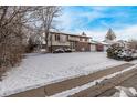 Two story home with brick and tan siding, a covered entry and a snow-covered yard and street in this winter scene at 1520 Phillips Dr, Northglenn, CO 80233