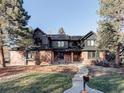 Two-story home with dark siding, brick accents, mature trees, and a walkway leading to the front door at 1 Winged Foot Way, Littleton, CO 80123