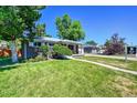 Well-maintained front yard of a brick home with mature trees, a sidewalk, and a 'For Sale' sign at 7011 Poplar St, Commerce City, CO 80022
