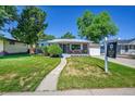 A charming single-story brick home with a lush lawn, sidewalk, mature trees, and a 'For Sale' sign at 7011 Poplar St, Commerce City, CO 80022
