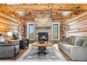 Living room featuring log walls, stone fireplace, hardwood floors, and comfortable seating at 1651 Pine Valley Rd, Evergreen, CO 80439