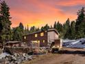 Beautiful home exterior against a vibrant sunset sky with a stone wall and surrounded by a lush forest landscape at 28268 Shadow Mountain Dr, Conifer, CO 80433