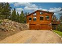 Wood cabin exterior with a two-car garage, stone retaining wall, and stairs leading to the side of the house at 310 Wendelyn Way, Boulder, CO 80302