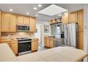 Well-lit kitchen featuring stainless steel appliances, tile countertops, a skylight and warm wooden cabinetry at 8468 Chase Dr, Arvada, CO 80003