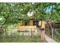 Charming two-story yellow home featuring a covered porch, mature trees, and fenced front yard at 7 Elati St, Denver, CO 80223