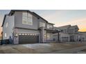 A two-story home showcases gray siding, stone accents and a two car garage with a concrete driveway during sunset at 6633 Bridlespur St, Castle Pines, CO 80108