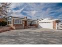 Home's brick facade featuring a well-maintained lawn, an attached two-car garage, and a large driveway at 8280 Queen St, Arvada, CO 80005