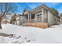 Gray home with a covered porch, brick foundation, and snowy yard, offering curb appeal at 2112 Springs Pl, Longmont, CO 80504