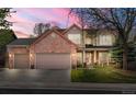 Charming two-story brick home featuring a three-car garage, covered porch, and well-maintained front yard at sunset at 13131 Pennsylvania St, Thornton, CO 80241