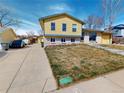 Charming yellow two-story home with a long driveway, trash receptacles and lawn with winter kill at 4487 S Alkire St, Morrison, CO 80465