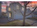 Two-story home featuring a white garage door, tan siding, manicured lawn, and a small garden area in front at dusk at 22150 E Berry Pl, Aurora, CO 80015