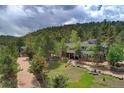 An elevated view showcases this property's verdant grounds with mature trees and brick accents against a wooded backdrop at 97 Soda Creek Rd, Evergreen, CO 80439