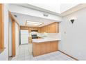 Bright kitchen featuring wood cabinets, white tile floors, and a pass-through to the living area at 1350 S Idalia St # G, Aurora, CO 80017