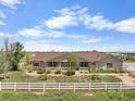 Tan ranch home with charming front porch and white fence in a serene setting with beautiful, mature trees at 32501 E 137Th Way, Brighton, CO 80603