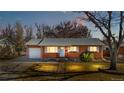 Charming red brick single story home featuring a attached garage, green front lawn, and mature trees at dusk at 6359 Brooks Dr, Arvada, CO 80004