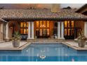 Outdoor pool with stone patio, view of house with pillars, doors, and window lit up from the inside at 45 Charlou Cir, Cherry Hills Village, CO 80111