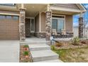 Inviting covered front porch with stone pillars and seating area, leads to front door at 5495 Espana Ct, Denver, CO 80249