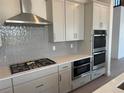 A close up of a kitchen with stainless steel range and double ovens surrounded by light grey backsplash and cabinets at 9382 Quaker St, Arvada, CO 80007