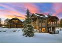 A luxurious mountain home featuring natural wood siding, stone accents, and a three car garage at sunset at 219 Glen Eagle Loop, Breckenridge, CO 80424
