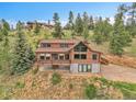 A wide exterior shot of a log cabin home that includes a deck, garage, and staircase at 25704 Shiloh, Conifer, CO 80433