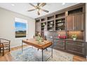 Bright home office featuring custom built-in shelving, a modern ceiling fan, and a wooden desk at 8784 S Riviera Ct, Aurora, CO 80016