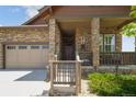 Inviting front porch featuring stone pillars and charming decor, adjacent to a three-car garage for convenience at 15804 Elizabeth E Cir, Thornton, CO 80602