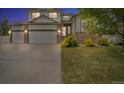 Charming two-story home at twilight featuring a three-car garage, stone accents, lush lawn and mature trees at 5286 Rustic Ave, Firestone, CO 80504