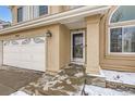 Close up of the front entrance of a tan home with a white garage door and covered porch at 9241 Roadrunner St, Highlands Ranch, CO 80129