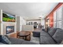 Open-concept living room featuring a fireplace, hardwood floors, and seamless access to the modern kitchen at 13884 Lilac St, Thornton, CO 80602