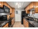 Galley kitchen with wooden cabinets, black appliances, granite countertops, and tile flooring at 8600 E Alameda Ave # 21-208, Denver, CO 80247