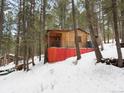 Charming cabin with a covered porch, surrounded by mature trees and a snowy landscape at 5525 S Twin Spruce Dr, Evergreen, CO 80439