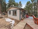 Quaint home exterior with a wooden walkway to a deck featuring red chairs and scenic mountain views at 26349 Pleasant Park Rd, Conifer, CO 80433