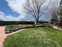 Expansive backyard features a lush lawn, stone-lined flowerbeds, mature trees, and a brick path at 12408 W 83Rd Ave, Arvada, CO 80005