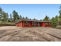 Daytime exterior of a charming red home featuring a well-maintained gravel driveway and natural landscaping at 4776 Red Rock Dr, Larkspur, CO 80118