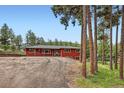 View of red home with ample parking space and mature trees, creating a serene and private setting at 4776 Red Rock Dr, Larkspur, CO 80118