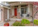 Inviting covered front porch with brick accents, cozy seating, decorative plants, and a bright red front door at 6614 W Gould Dr, Littleton, CO 80123