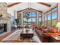 Spacious living room features a stone fireplace, wood beams, and panoramic views through large windows at 6169 Flat Creek Dr, Evergreen, CO 80439
