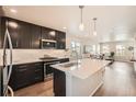 Open kitchen with dark cabinets, stainless appliances, large island, and wood floors at 12770 Tamarac St, Thornton, CO 80602