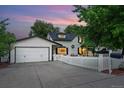 View of home and detached garage, with mature trees, white picket fence, and wide driveway at 6830 Lamar St, Arvada, CO 80003