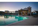 Community pool with modern clubhouse featuring lounge chairs and seating areas at dusk at 8628 Hotchkiss St, Littleton, CO 80125