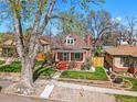 Quaint two-story brick home with a red roof and front porch offers a charming view nestled among mature trees at 2772 Julian St, Denver, CO 80211