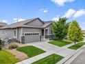 Lovely gray home featuring stone accents, an attached garage, and lush green lawn space at 18036 E 99Th Ave, Commerce City, CO 80022