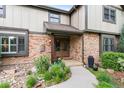 Inviting entrance featuring a tiled porch, brick facade, manicured garden, and a wooden front door at 5185 W Fair Pl, Littleton, CO 80123