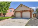 Attached two-car garage with brick accents, a paved driveway, and landscaping at 4548 Gibraltar Way, Denver, CO 80249