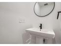 Modern powder room featuring a pedestal sink with a round mirror, white walls and fixtures, exuding simplicity at 10157 W 38Th Ave, Wheat Ridge, CO 80033