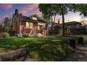 Dusk view of a charming brick home featuring a well-maintained lawn and mature trees, creating a warm, inviting atmosphere at 1260 S Emerson St, Denver, CO 80210
