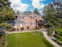 View of the red brick two-story home with gray roof and mature trees around the green grass yard at 5428 Golden Currant Way, Parker, CO 80134