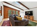 Bright living room with wood-paneled walls, exposed beams, a skylight, and a large sectional sofa at 7221 S Brook Forest Rd, Evergreen, CO 80439