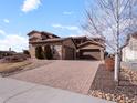 Stunning home exterior with stone accents, a three-car garage, and a brick driveway at 9355 E Winding Hill Ave, Lone Tree, CO 80124