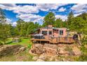 Charming exterior with a spacious deck, outdoor seating, and a hot tub nestled among natural rock formations at 8838 Hillview Rd, Morrison, CO 80465